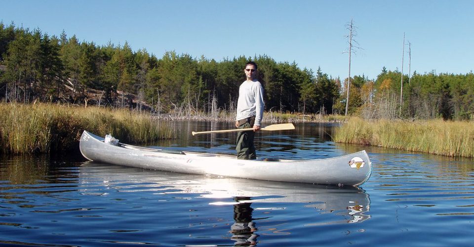 Man standing in canoe on river. A\J AlternativesJournal.ca